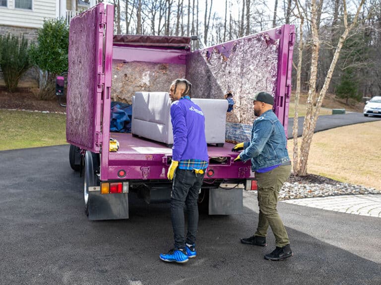 People loading a sofa into a junk removal truck