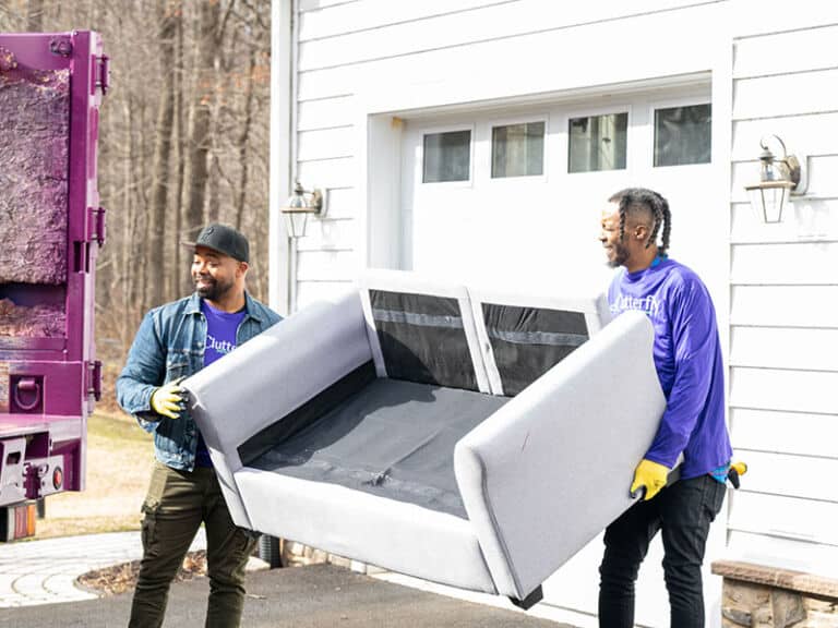 Two men carrying a sofa to a Clutterfly Junk Removal truck
